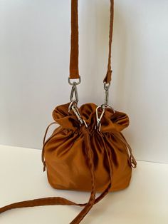 Dimensions H 28 cm/ 11 in  W 22 cm / 8.6 in D 10 cm /  3.9 in Materials Dark bronze  color Satin Fully lined in beige  color satin. Drawstring closure.  Detachable top handle and long strap. Dark bronze satin small bag. The mouth of the bag made of satin  is closed by squeezing.  The handles made of the same satin fabric are mounted on the bag with silver-colored metals. Four metal feet in silver color on the base protect the bag from dirt when placed on the floor. A special material is used bet Gold Pouch-shaped Bucket Bag For Evening, Gold Pouch-shape Evening Bucket Bag, Bucket Evening Bag With Handles, Pouch Bucket Bag With Handles For Evening, Brown Handheld Evening Bag For Travel, Evening Brown Bucket Bag With Detachable Strap, Formal Handheld Brown Bucket Bag, Brown Crossbody Bucket Bag For Evening, Evening Brown Crossbody Bucket Bag