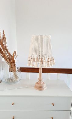 a white dresser topped with a lamp and vase filled with dried flowers on top of it