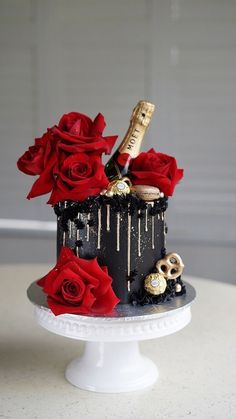 a black cake with red roses and wine bottle on top is sitting on a white pedestal