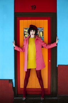 a woman standing in front of a door wearing a pink coat and red tights