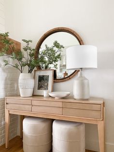 a white vase sitting on top of a wooden table next to a mirror and plant