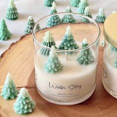 two candles sitting next to each other on top of a wooden table covered in frosted trees