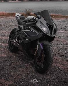 a black motorcycle parked on top of a gravel field next to a body of water