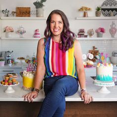 a woman sitting at a counter with cakes and cupcakes