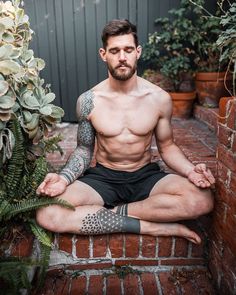 a shirtless man sitting in the middle of a brick wall with tattoos on his arms and legs