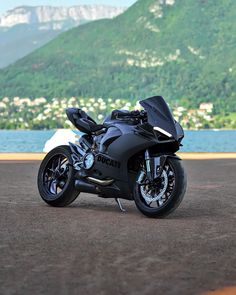 a black motorcycle parked next to a body of water with mountains in the back ground