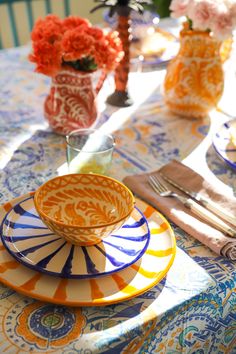 an orange and blue plate sitting on top of a table next to vases filled with flowers