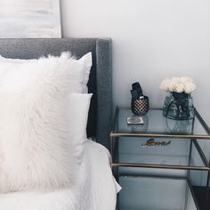 a bed with white sheets and pillows next to a night stand on top of a glass table