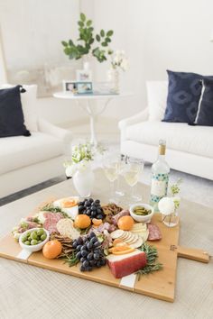 a wooden tray topped with fruit and cheese on top of a table next to two white couches