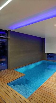 an indoor swimming pool with wooden flooring and blue lights on the ceiling above it