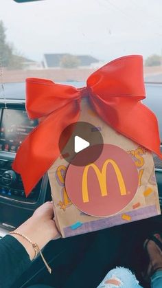 a person holding up a mcdonald's bag with a red bow on it in their car