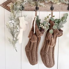 two stockings hanging from hooks on a wall with greenery and pine cones in them