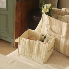 two storage bags sitting on top of a bed next to a vase with flowers in it