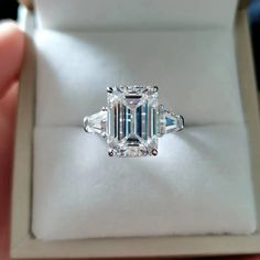 an emerald cut diamond ring in a white box with its reflection on the inside of it