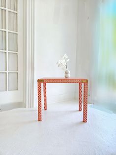 an orange and white table with flowers on it in front of a large window,