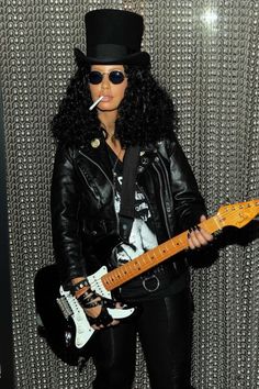 a woman with long black hair and a top hat holding a guitar in front of a wall