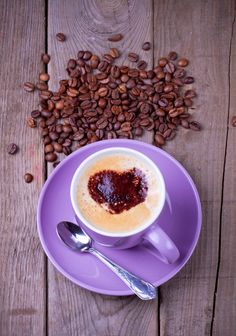 a cup of coffee with saucer and spoon on purple plate next to roasted coffee beans