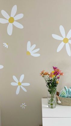 a white dresser topped with a vase filled with flowers next to a wall painted with daisies