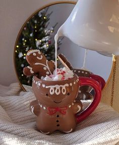 a cup filled with hot chocolate and marshmallows next to a christmas tree