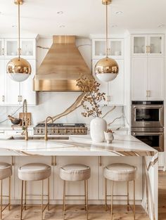 a white kitchen with gold accents and marble counter tops, an island in the middle