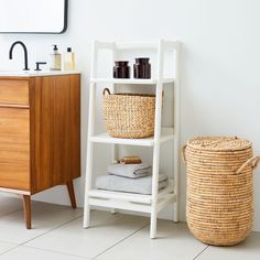 a white shelf with baskets and towels on it next to a wooden cabinet in a bathroom