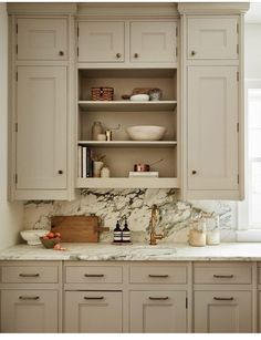 a kitchen with white cabinets and marble counter tops, along with an open shelf above the sink