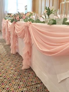 the table is covered with pink chiffon draping and floral centerpieces