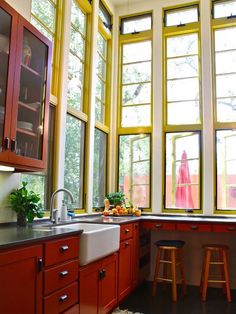 a kitchen with lots of windows and wooden cabinetry, along with stools in front of the sink