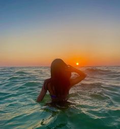 a woman sitting in the water at sunset with her back to the camera, looking into the distance