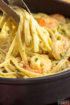 a fork full of pasta with shrimp and parmesan cheese in a skillet