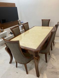 a dining room table with chairs and a television on the wall in the back ground