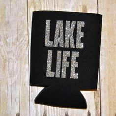 a black can cooler with the words lake life printed on it sitting on a wooden surface