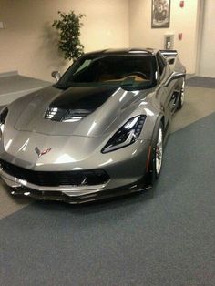 a silver sports car is parked in a showroom with other cars on the floor