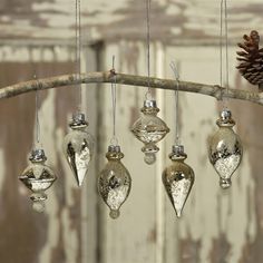 an assortment of glass ornaments hanging from a branch with a pine cone in the background