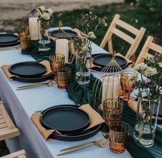 the table is set with black plates and vases, gold candlesticks, and green napkins