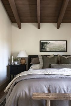 a bed sitting under a wooden ceiling next to a night stand with two lamps on top of it