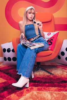 a woman is sitting on an orange chair with a magazine in her lap and holding a cell phone