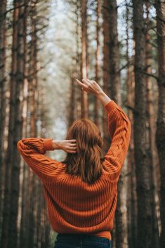 a woman standing in the middle of a forest with her hands on her head and arms behind her back