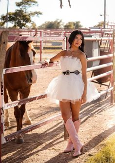 a beautiful young woman standing next to a horse in a corral with her hand on the gate