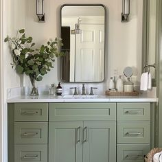 a bathroom with green cabinets and a large mirror on the wall over the sink, along with a vase filled with flowers