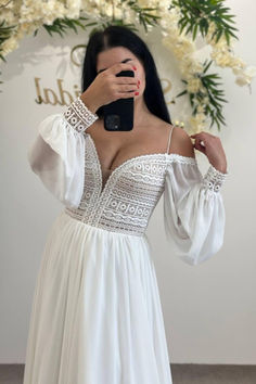 a woman taking a selfie in front of a floral wreath wearing a white dress