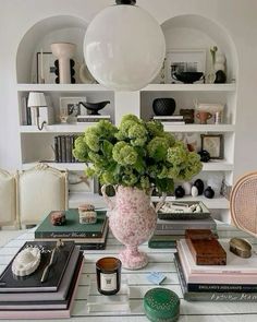 a table topped with lots of books next to a vase filled with flowers and plants