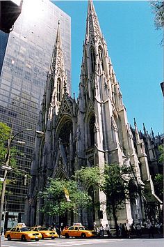 the cathedral is very tall and has many spires on it's sides as well as yellow cabs parked in front