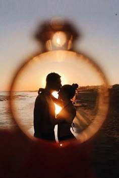 a man and woman standing next to each other in front of the ocean at sunset