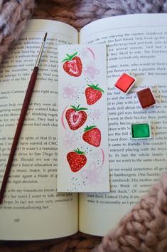 an open book with strawberries on it next to some wax cubes and a pencil