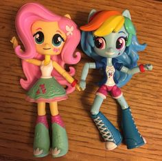 two little pony dolls standing next to each other on top of a wooden table together