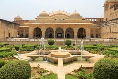 an ornate courtyard with water fountain surrounded by greenery and shrubs in the foreground