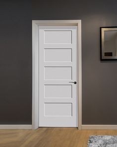 an empty room with a white door and rugs on the wooden floor next to it