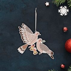 two birds are hanging from a christmas ornament on a black surface next to ornaments