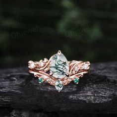 a green and white stone ring sitting on top of a piece of wood with leaves around it